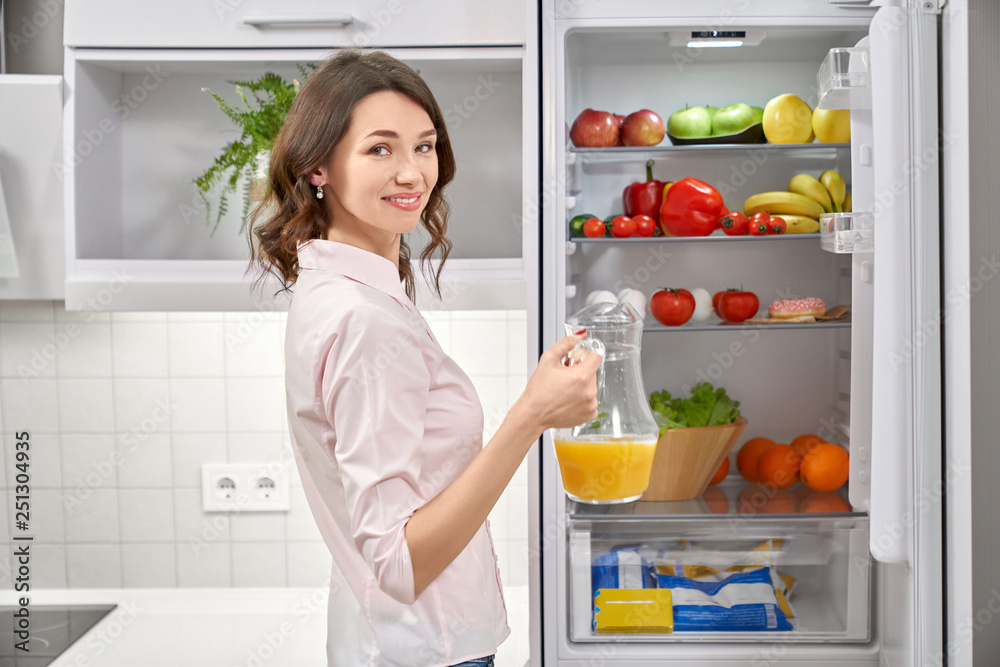 Woman opening refrigerator, holding pitcher with juice. Woman opening refrigerator, holding pitcher with juice.