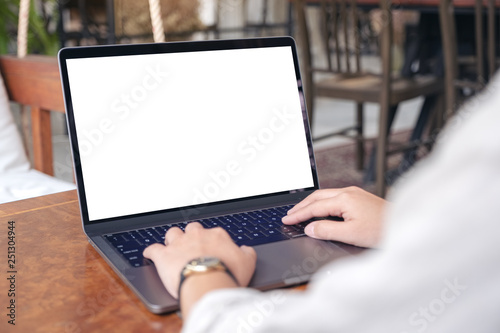 Mockup image of a woman using and typing on laptop with blank white screen on wooden table