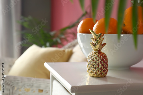 Golden pineapple with oranges on white table in room