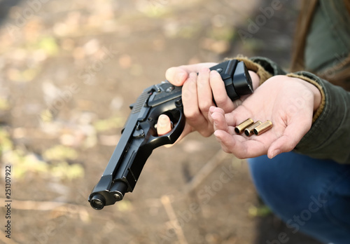 Young depressed woman with gun and bullets thinking about suicide outdoors