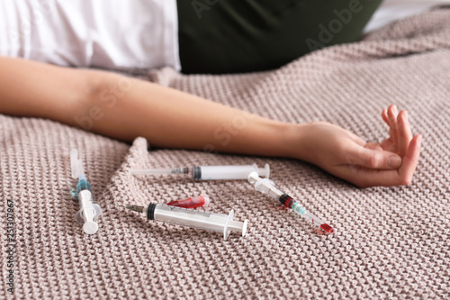 Young unconscious woman with syringes lying on bed. Suicide concept