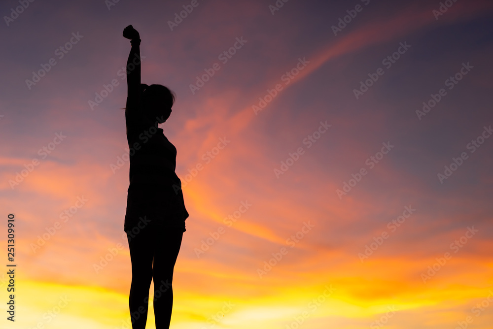 The silhouette of the woman is standing, holding hands relaxed with success at sunset.