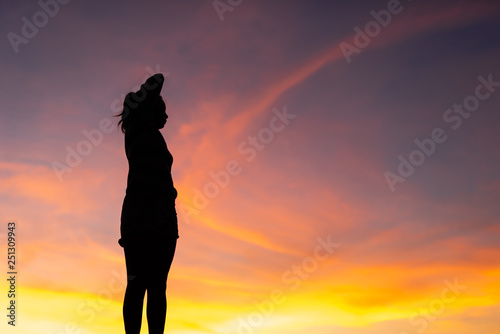 The silhouette of the woman is standing, holding hands relaxed with success at sunset.
