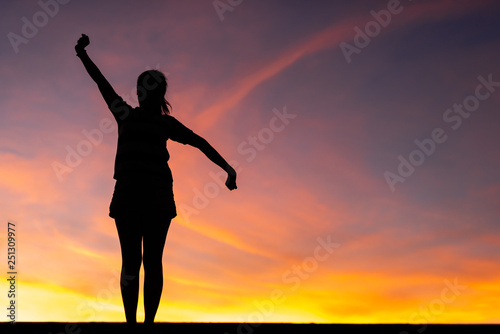 The silhouette of the woman is standing, holding hands relaxed with success at sunset.