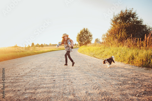 happy child girl enjoying summer vacations with her dog, walking and playing on sunny meadow. Traveling, exploring new places and rural living concept