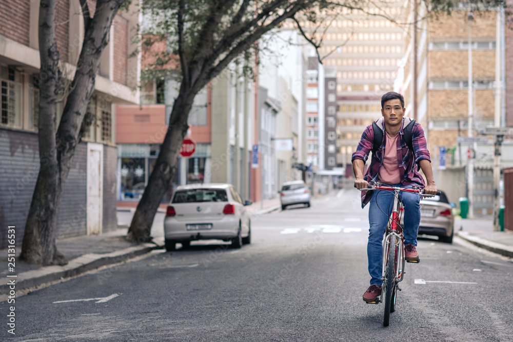 Young Asian man riding his bike along a city street