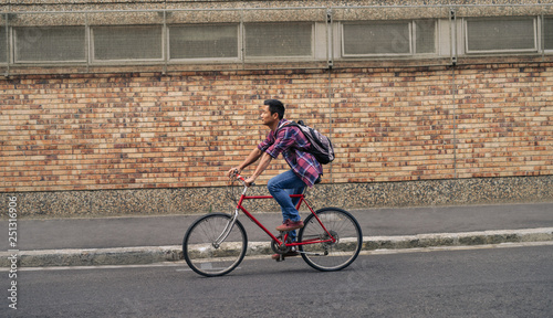 Fototapeta Naklejka Na Ścianę i Meble -  Young Asian man riding his bicycle down a city street