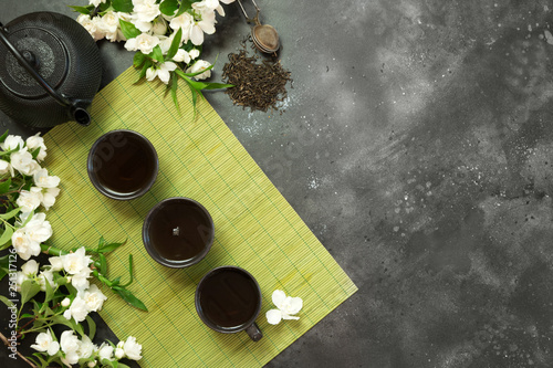 Green jasmin tea and jasmine flowers, cup of green tea on black. Top view. Teatime.