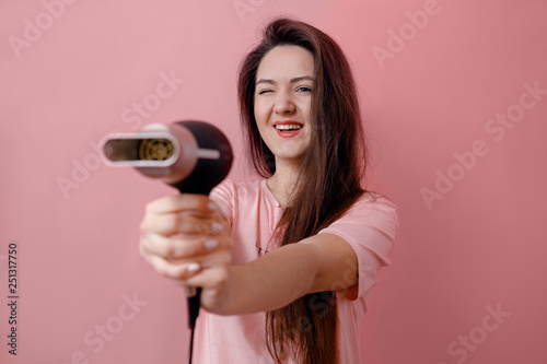 young smiling woman like gangster with hairdryer in hands on pink background