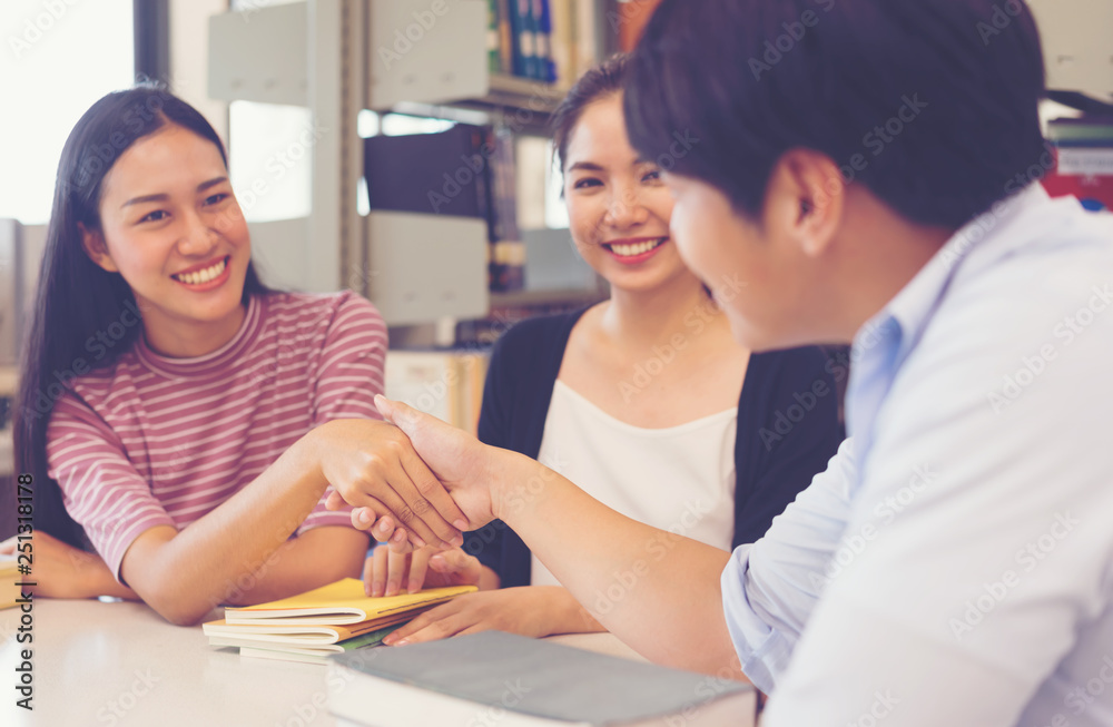 College students happy to meet his friend and shaking hands in library. College students happy to meet his friend and shaking hands in library.