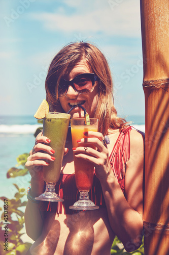 Beautiful woman drinking cocktail and using cellphone on the tropical sandy beach.