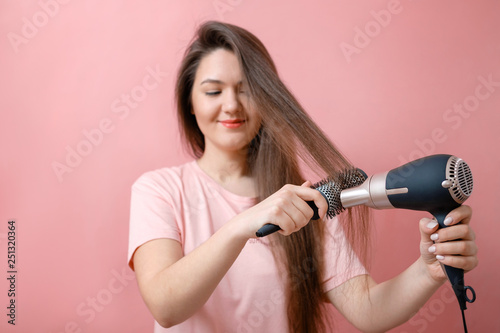 young smiling woman with hairdryer in hands on pink background