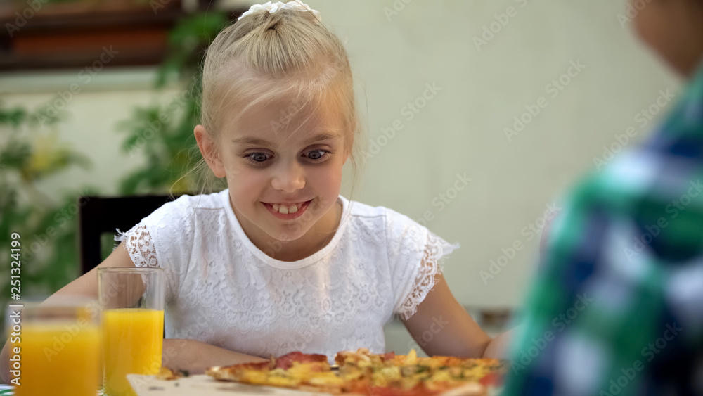 Smiling girl looking at pizza and choosing best slice, family food traditions Smiling girl looking at pizza and choosing best slice, family food traditions