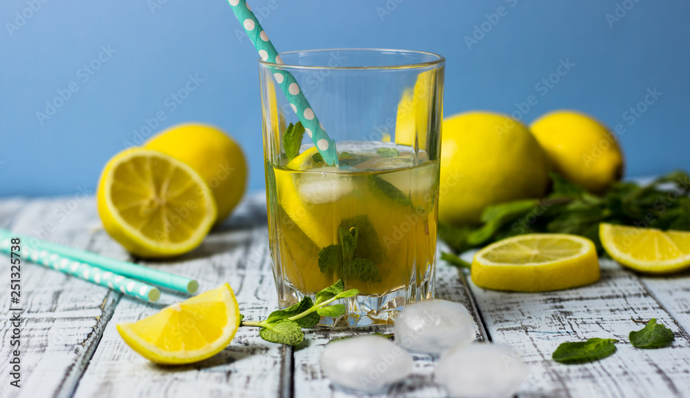 Summer refreshing drink in a glass. Traditional cold sweet-sour lemonade with lemon, mint and ice cubes on a gray wooden table.