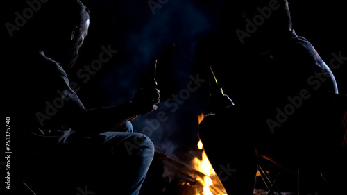 Two friends sitting around open fire at night and drinking beer, relaxing time