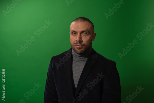 Studio fashion portrait in monochrome. Elegant young handsome serious man iin studio with green background.