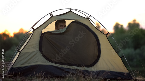 Joyful man zipping dome tent, preparing to sleep in wild, comfortable rest