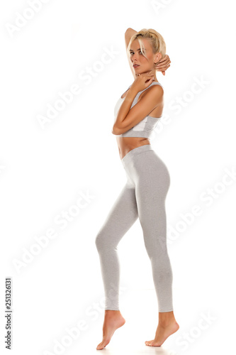 Side view of slim sporty young woman in gray leggings on white background