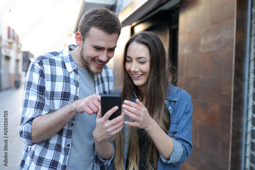 Happy friends or couple using a smart phone in the street Happy friends or couple using a smart phone in the street