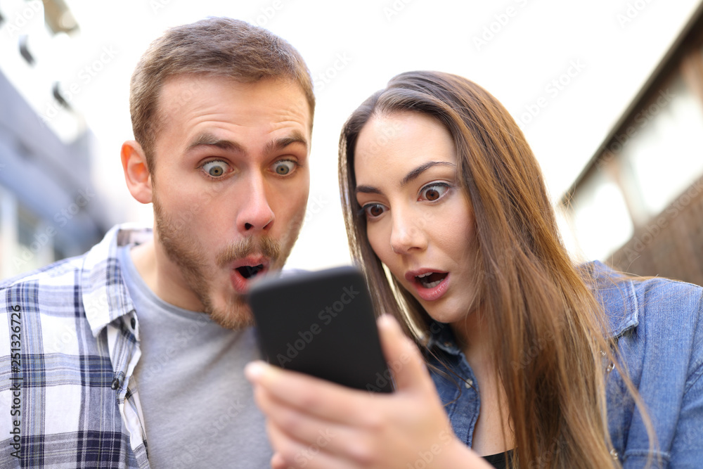 Surprised couple checking online news on smart phone Surprised couple checking online news on smart phone