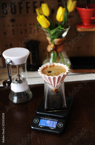Alternative coffee brewing. Pink ceramic dripper with paper filter. Electronic scale. Yellow tulips on the background
