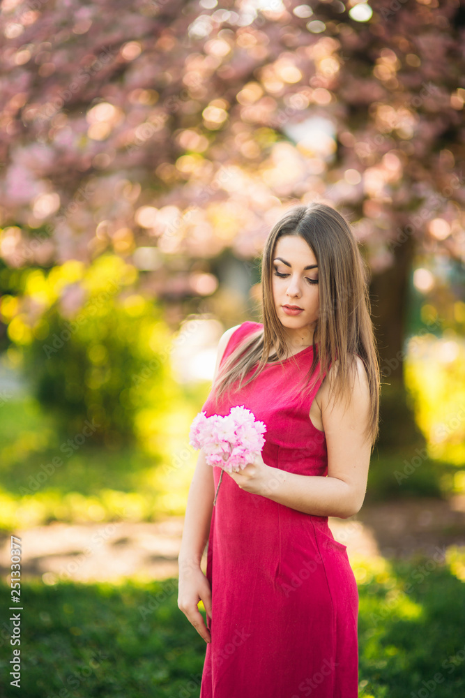 Portrait of charming girl in a fuchsia dress. She hold a flowers of sakura in her hands. Background of sakura tree Portrait of charming girl in a fuchsia dress. She hold a flowers of sakura in her hands. Background of sakura tree