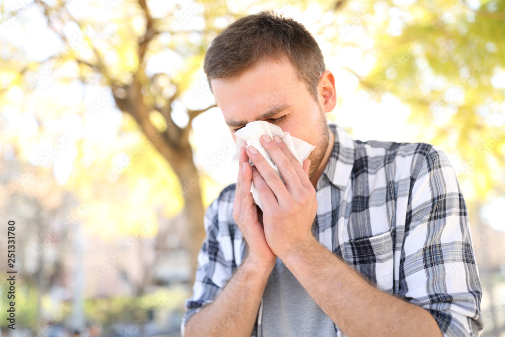 Allergic man sneezing covering nose with wipe