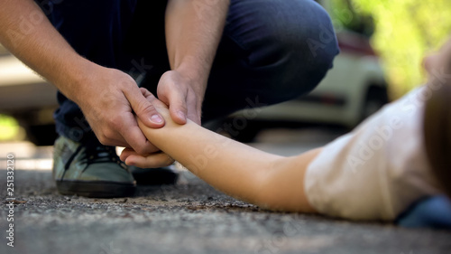 Tableau sur toile Man holding hand of girl lying on road, unconscious victim of car accident, 911