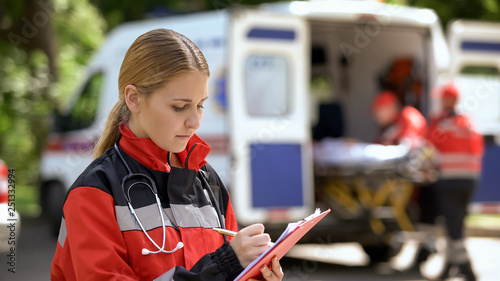 Female doctor keeping medical records, ambulance crew transporting patient