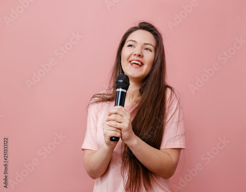 young funny woman with microphone in hand on pink background