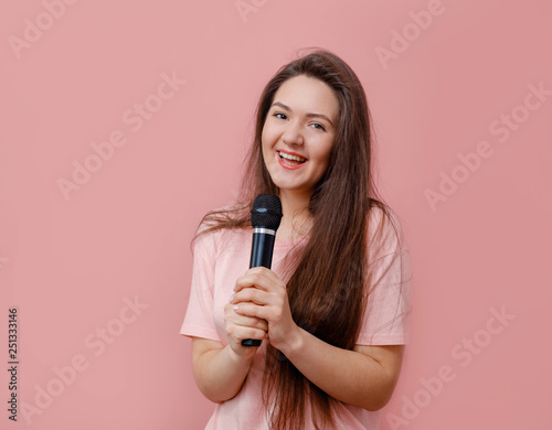 young funny woman with microphone in hand on pink background