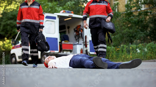 Ambulance crew running to man lying on road, first aid at car accident scene