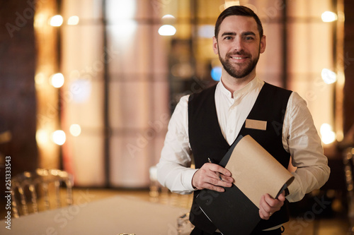 Waist up portrait of handsome waiter smiling cheerfully at camera standing in luxury restaurant or cafe, copy space photo