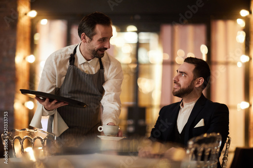 Portrait of mature waiter bringing coffee to client in luxury restaurant, copy space