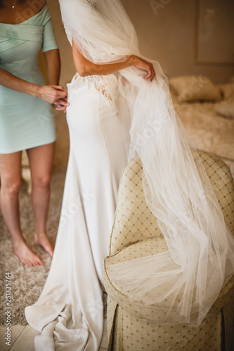 A bridesmaid is tying up brides gown from the back.