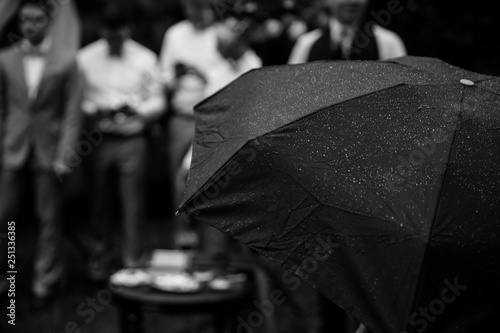 A big black umbrella on the foreground. Four man standing on the background.
