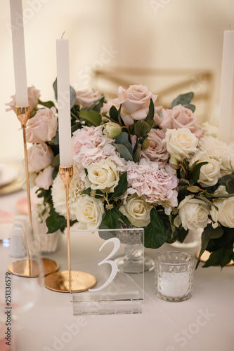 A flowers bouquet standing at the table alongside with some candles and a nuber 3 sign. photo