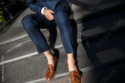 A groom is sitting at the steps. He is wearing a blue suit and a brown shoes.