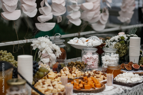 A bunch of desserts and some flower bouquets are standing on a served table.