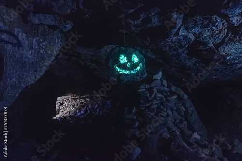 Dark creepy glowing phosphorescent smiling face on hanging stone in cave
