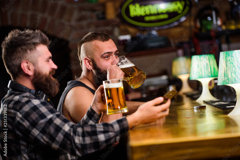 Men drinking beer together. Hipster brutal man drinking beer with friend at bar counter. Men drunk relaxing having fun. Alcohol drinks. Friends relaxing in pub with beer. Refreshing beer concept