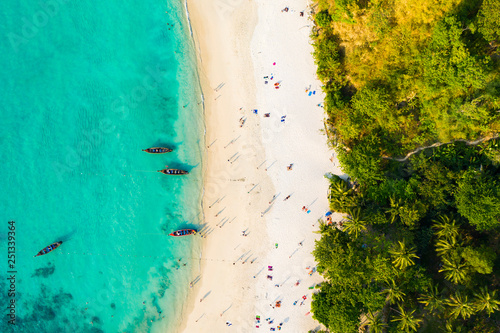 View from above, aerial view of a beautiful tropical beach with white sand and turquoise clear water, longtail boats and people sunbathing, Freedom beach, Phuket, Thailand.