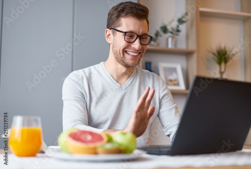 Excited man using laptop sitting at table with fruit 