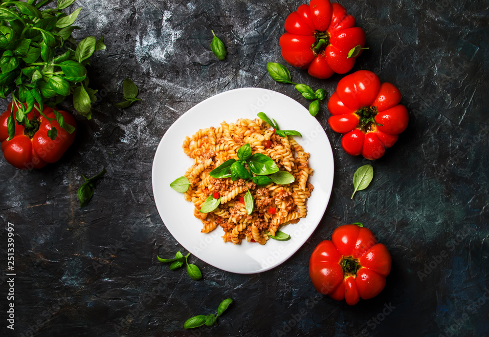 Tasty pasta with minced meat and tomato sauce with green basil on white plate, dark background kitchen table, top view Tasty pasta with minced meat and tomato sauce with green basil on white plate, dark background kitchen table, top view