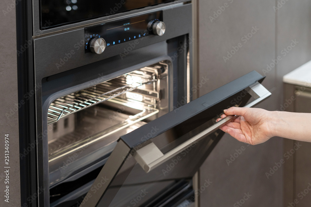 Woman hand opening builtin oven in black kitchen Stock Photo