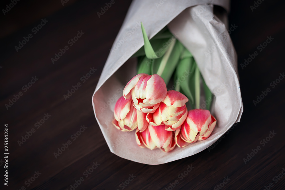 Five roses in a peach-colored kraft paper on a dark wooden background, natural light, horizontal arrangement