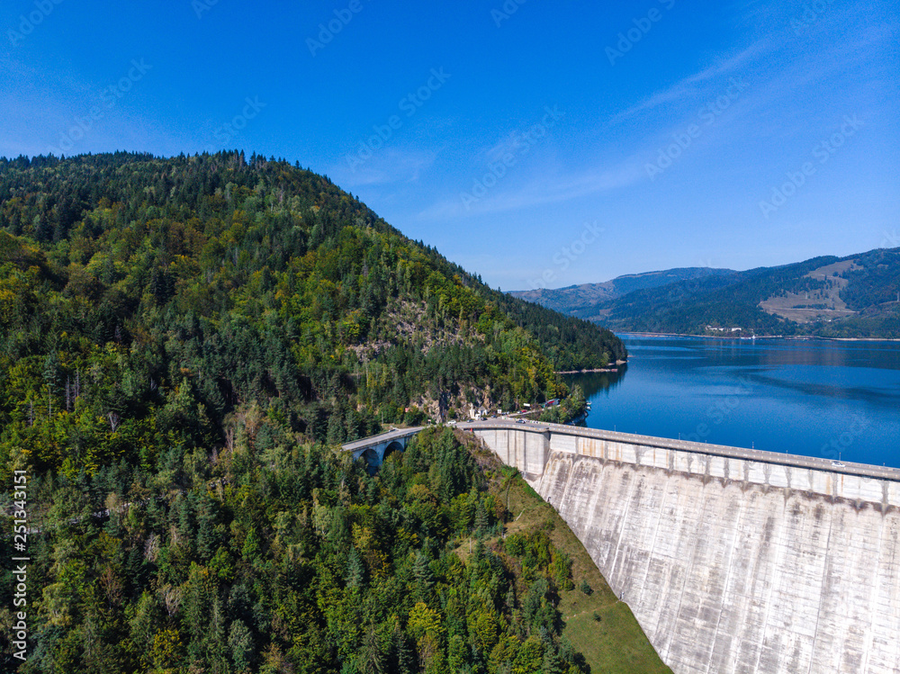 Aerial scenic view of a dam constructed on a beautiful valley in mountains. water storage reservoir. road with beautiful views for travel and holidays. lake Lzvorul Muntelui, Romania.