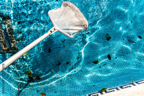 Maintenance man using a pool net leaf skimmer rake in summer to leave ready for bathing his pool.