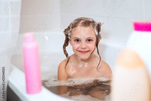 happy  little girl of 6 years old (babe) sits in the bathroom in the water with fluffy foam, washes her head herself using a shampoo without tears that does not pinch the eyes