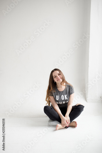 Portrait of a smiling young girl sitting with legs crossed isolated on white background. happy young girl in torn jeans and gray t-shirt isolated on white